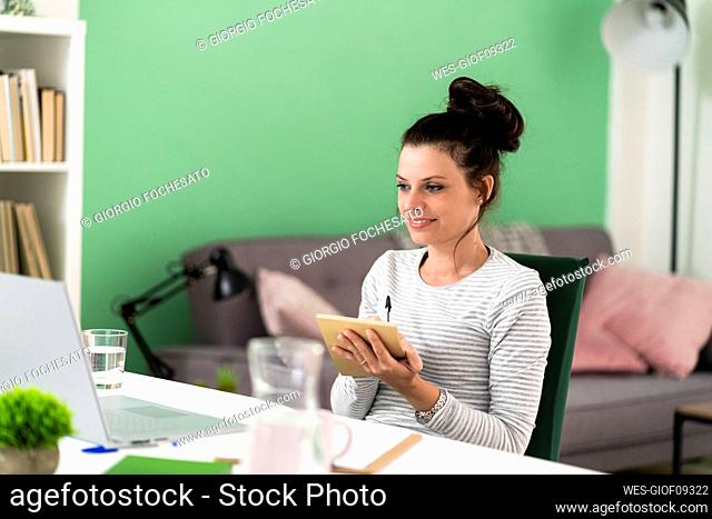 Woman writing in note pad while sitting on chair at home