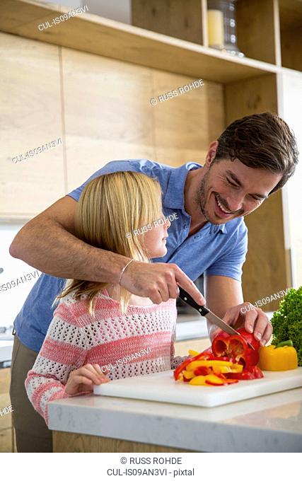 Man teaching daughter to slice vegetables on kitchen counter