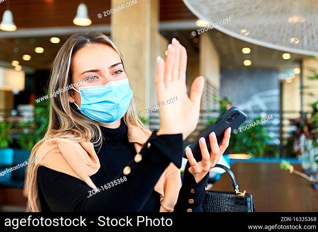 Frau im Restaurant mit Mundschutz winkt zur Begrüßung auf Distanz wegen Covid-19