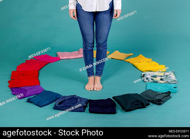 Young woman standing inside circle made of colorful clothes against blue background