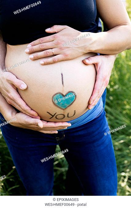 Hands of expectant parents stroking baby belly outdoors