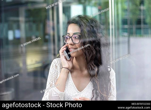 Close-up of woman with long hair talking over mobile phone while standing against window