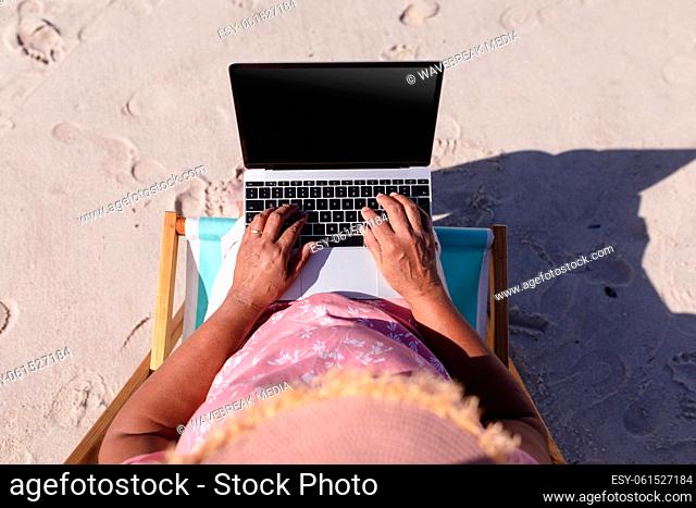 Overhead view of senior african american woman using laptop while sitting on deck chair at the beach