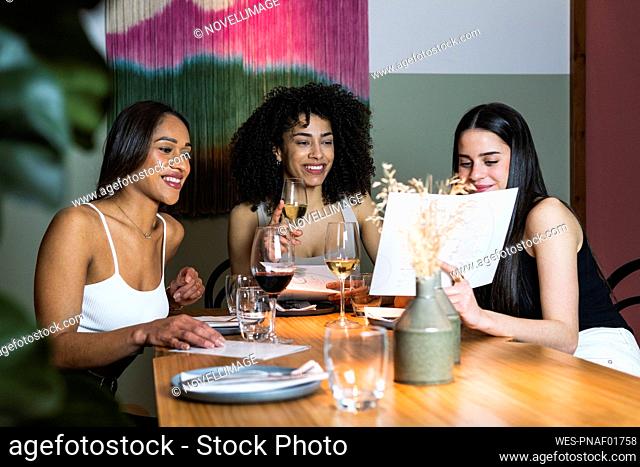 Woman showing menu to friends while having drink in restaurant