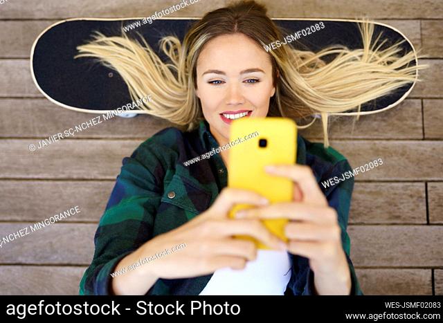 Smiling woman using mobile phone while lying down on skateboard