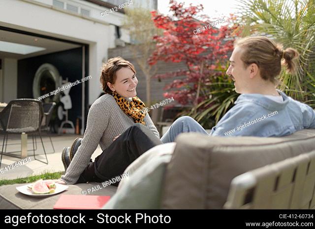 Happy young couple talking on sunny patio lounge chair