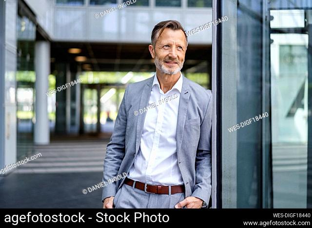 Contemplative businessman with hands in pockets leaning on wall