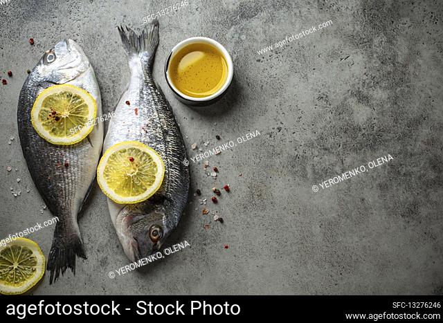 Raw fresh fish dorado with lemon wedges, olive oil and seasonings