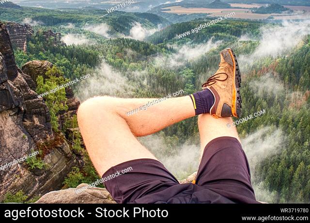 Hiker legs climbing on sunrise mountain peak rock. Slim legs of a mountain hiker with hiking boots on exposed rock