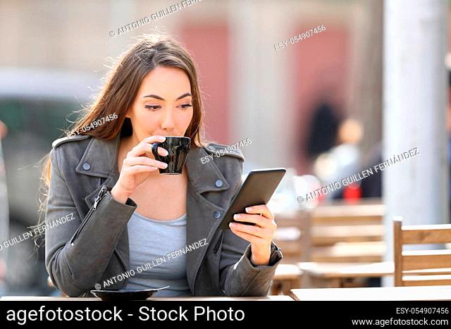 Portrait of a young woman drinking a cup of coffee checking her smart phone on a cafe terrace