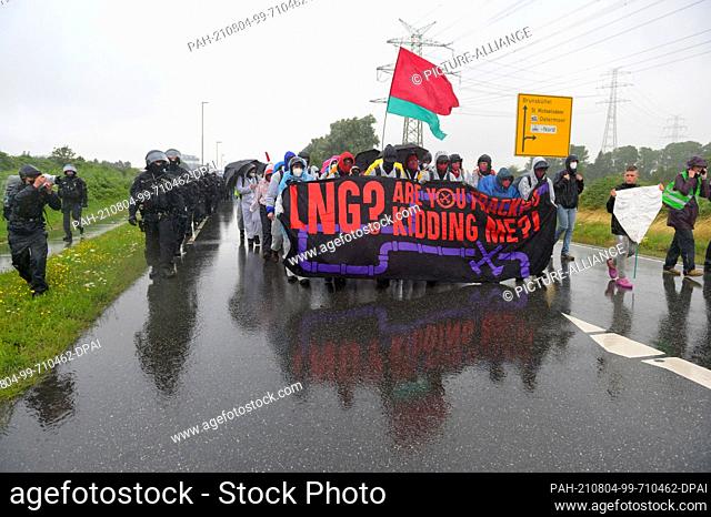 31 July 2021, Schleswig-Holstein, Brunsbüttel: Activists, accompanied by police, walk through ChemCoastPark with a placard reading ""LNG? Are you fracking...