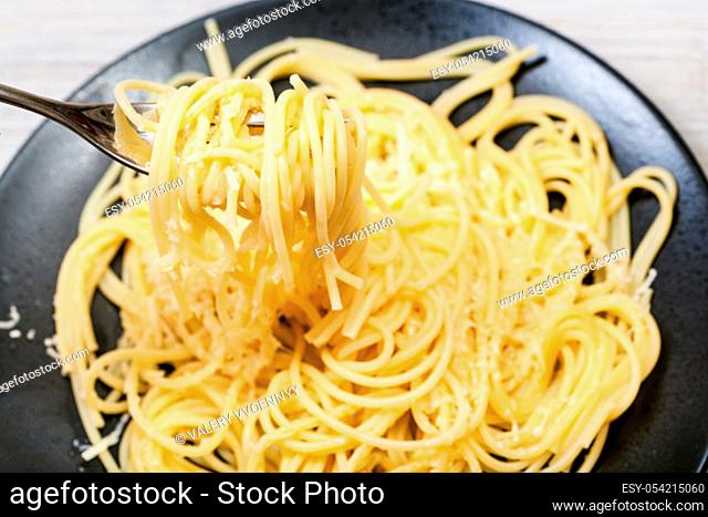 top view of fork with spaghetti al burro e parmigiano (pasta with butter and cheese) close up over black plate on gray wooden table