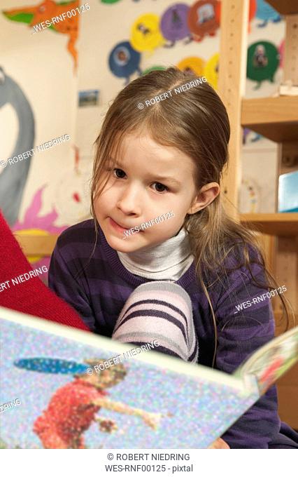 Germany, Girl 4-5 in nursery reading a book, portrait