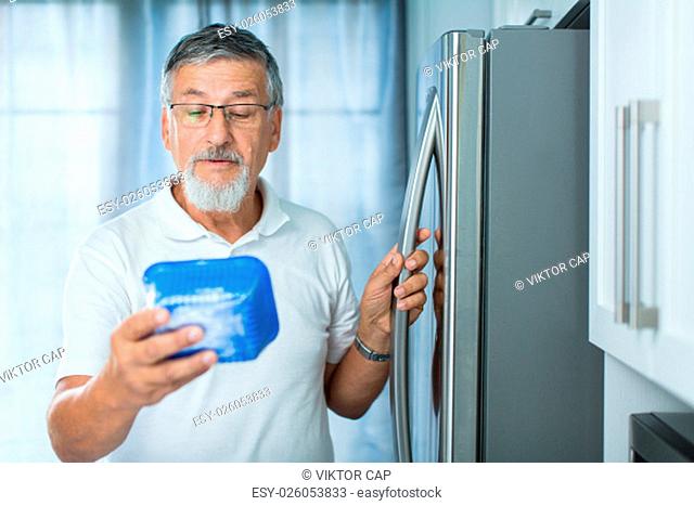 Is this still fine? Senior man in his kitchen by the fridge, looking at the expiry date of a product she took from her fridge -