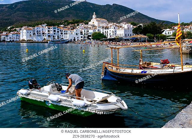Woman in Inflatable boat next to traditional sailing boats called "llagut" moored in front of white village of Cadaqués. Girona province, Catalonia, Spain