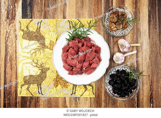 Plate of raw goulash, dried figs, plum and garlic bulbs on wooden background