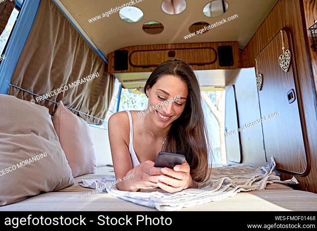 Smiling woman using mobile phone lying in motor home