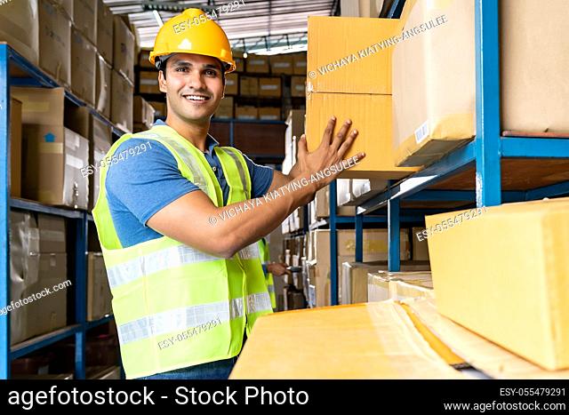 Indian warehouse worker put cardboard box in to shelf with muslim Islam asian worker do inventory in warehouse distribution center environment