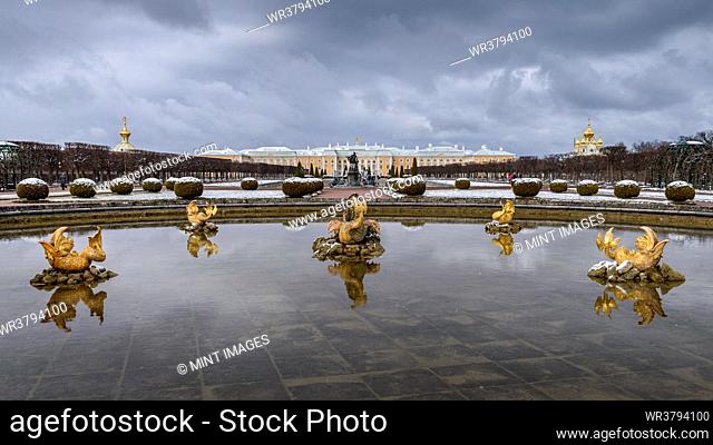 The facade of the Peterhof summer palace of the Romanov Tzars, fish fountains and still clear water, a light snow on topiary bushes