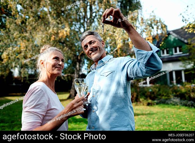 Smiling man holding champagne flute and house key by woman at backyard