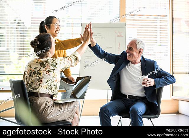 Happy business colleagues giving high-five to each other at work place