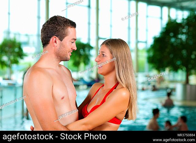 Two young people - a couple - at a public swimming pool standing in front of the water
