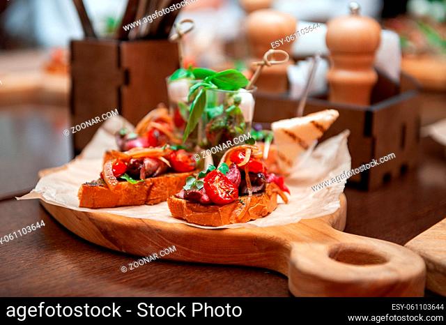 Tasty tomato Italian bruschetta on toasted slices of baguette with spice herbs and basil on a wooden board. Catering concept