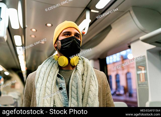 Man wearing protective face mask and headphones looking away while standing in train