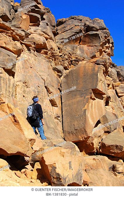 Tourist looking at the prehistoric petroglyphs on the rocks in Wadi Mathendous, Mesak Settafet Plateau, Libya, Africa