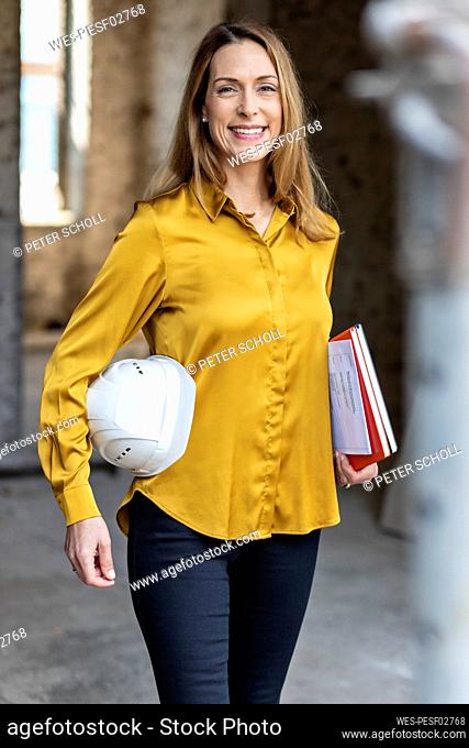 Smiling female architect holding hardhat while standing at construction site
