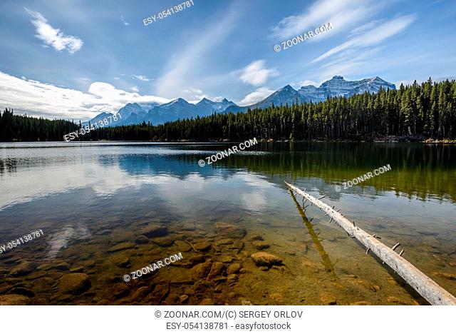 The sun is rising above the Herbert Lake and lighting up underwater stones and distant Rocky Mountains of Alberta, Canada