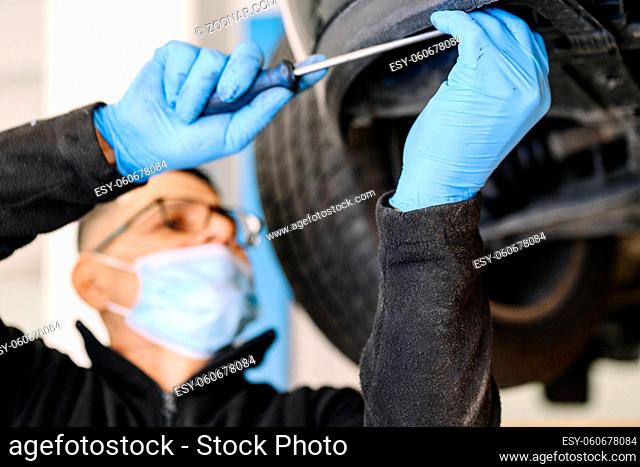 Professional mechanic with protective face mask, repairing a car in service garage. High quality photo