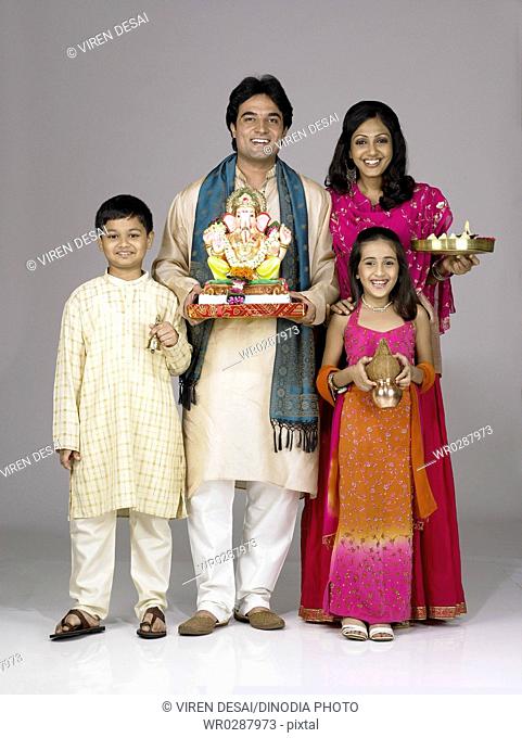 South Asian Indian family with father mother son and daughter holding statue of lord Ganesha and Kalash Aarti thali MR 698 , 699 , 700 , 701