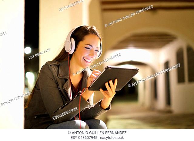 Woman watching and listening media on tablet in the night in the street