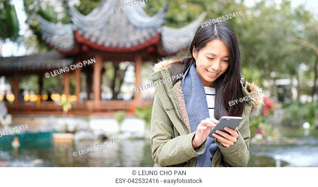 Asian Woman use of mobile phone in china, Chinese pavilion garden, woman wearing winter jacket