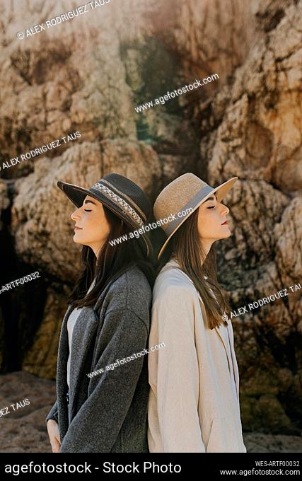 Female twins back to back standing by rock formation