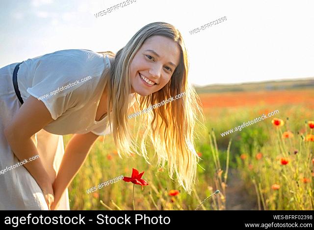Smiling blond woman by poppy flowers on field