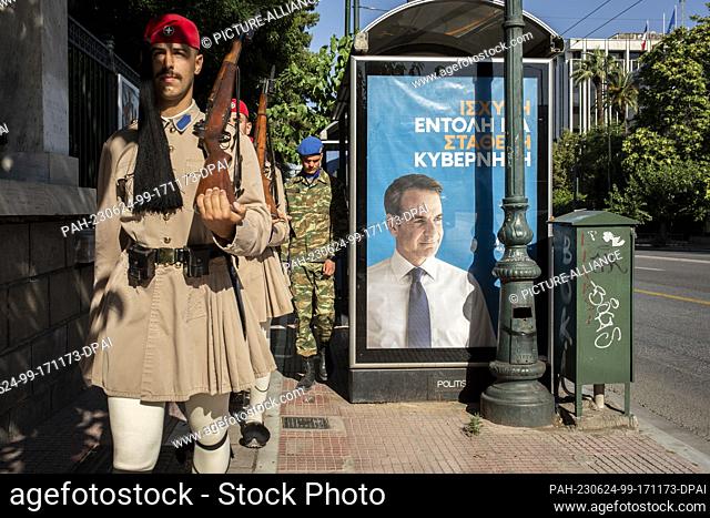 24 June 2023, Greece, Athen: National guardsmen walk past an election poster of party leader Mitsotakis of the conservative New Democracy party in the center of...