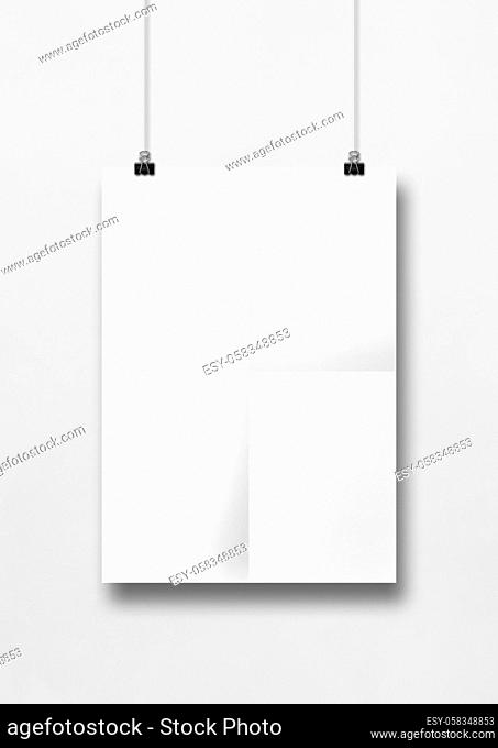 White folded poster hanging on a clean wall with clips. Blank mockup template