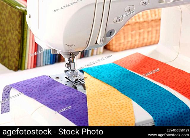 Sewing machine with a strips of fabrics on the background of stack of colorful quilting fabrics