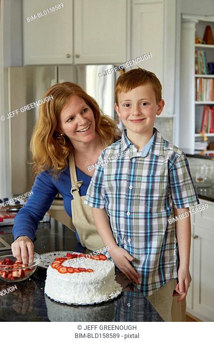 Caucasian mother and son decorating cake in kitchen