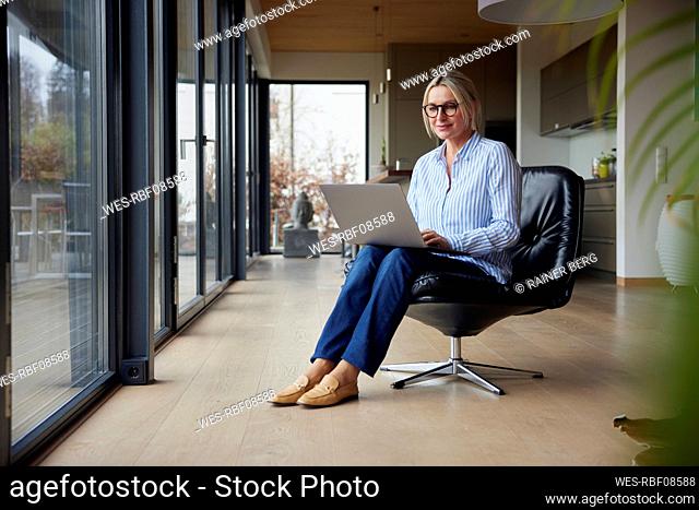 Woman using laptop sitting on chair at home