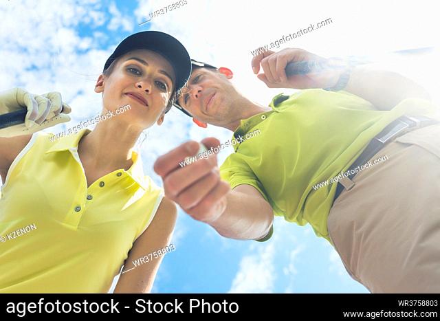 Low-angle view portrait of a young woman smiling while looking at camera during professional golf game with her partner or instructor outdoors