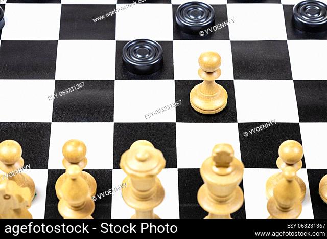 playing by different rules on the same board - black checkers and white chess figures on black white chessboard, above view of pawn and checkers piece moves...