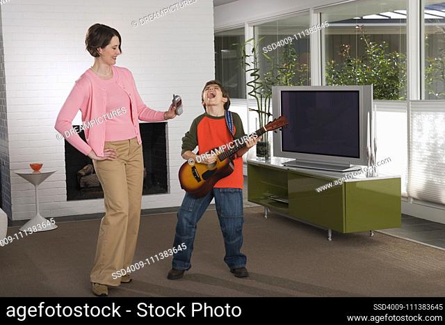 Mother holding telephone up to son playing guitar