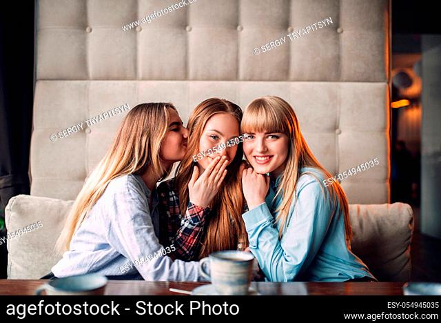 Three attractive girlfriends hugs together in cafe. Female friends sitting in restaurant on couch and drinks coffee, gossipers meeting