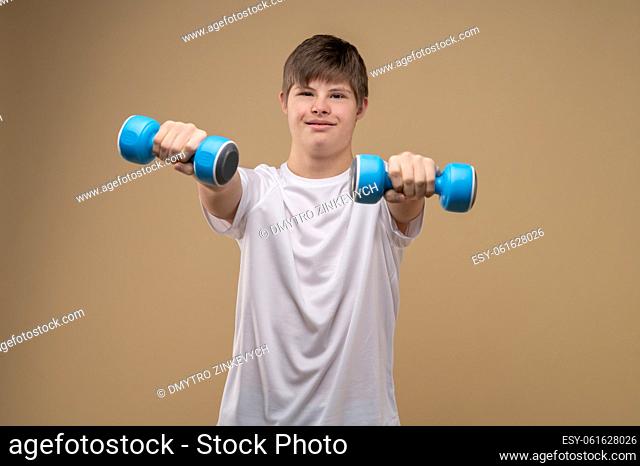 Waist-up portrait of a boy performing the dumbbell front raise in front of the camera