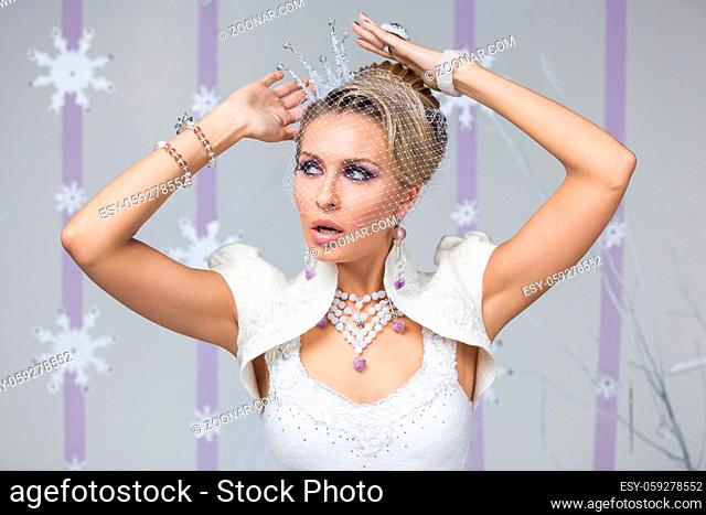 Beautiful young woman with purple makeup, fancy hairdo and small crystal crown on head. Gorgeous winter bride in felting dress with surprised expression