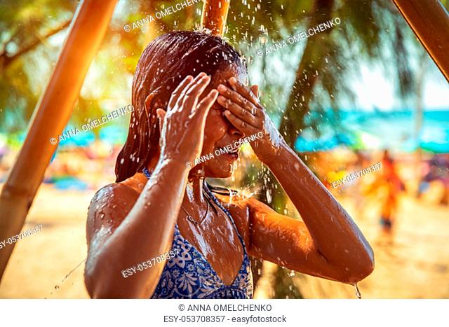 Little girl taking shower on the beach, pretty child with pleasure refreshing in cold water, enjoying summer vacation on the beach resort