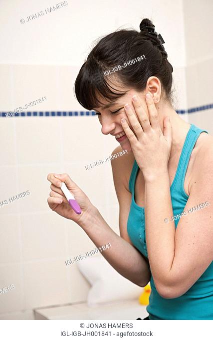 This picture shows a young caucasian woman with brown hair smiling as she watches a pregnancy test